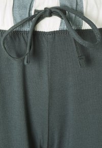 Dunkelgrüne Hose aus weicher Baumwolle mit einem elastischen Bund und einer dekorativen Schnur, gefertigt aus glattem, strukturiertem Stoff.