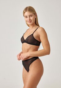 Zwart lingerie set met een sheer driehoekige bralette met verstelbare bandjes en een bijpassende hooggewaist thong. Gladde textuur en minimalistisch ontwerp.