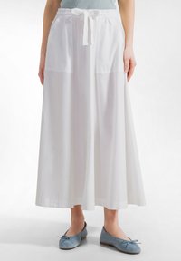 Kvinde iført en lang hvid nederdel med forlommer og snøre i taljen, kombineret med lyseblå ballet flats med sløjfer.