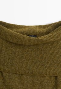Pull en tricot duveteux vert olive avec un large col bateau et une petite étiquette noire à l'intérieur du col.