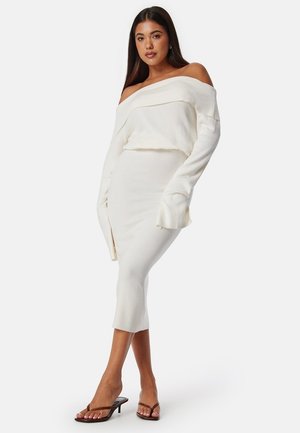 Off-shoulder vit stickad tröja tillsammans med en matchande midiklänning som har en sidoklyvning och texturerat tyg med långa ärmar.