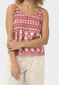 Lehký top bez rukávů v červené a krémové barvě, s propracovanými vzory a křížovým designem ramínek na výstřihu.