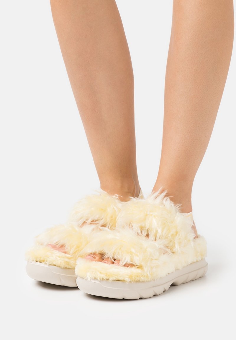 Furry yellow slide sandals with dual straps, soft texture, and a plush exterior; features a thick, white cushioned sole.