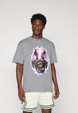 Grå bomulds T-shirt med et stort, farverigt grafisk motiv i midten. Designet inkluderer flammer og et logo. Modellen har lette shorts på.