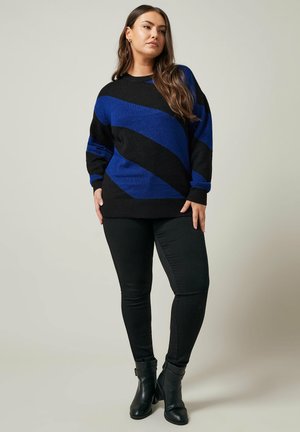 Gestreifter Pullover in Schwarz und Blau mit lockerer Passform, langen Ärmeln und gerippten Bündchen, kombiniert mit schwarzen Skinny-Jeans und Stiefeletten.