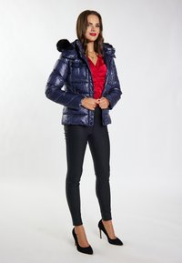 Giubbotto imbottito blu navy con cappuccio in pelliccia sintetica, con un design trapuntato. Abbinato a pantaloni neri aderenti e tacchi alti neri. Top rosso sotto.