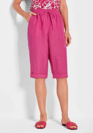 Roze linnen capri-broek met een trekkoord in de taille, opgerolde mouwen en zijzakken, gecombineerd met geweven roze slippers.