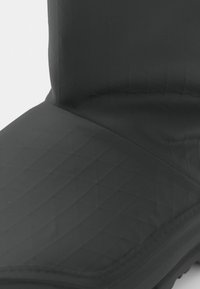 Bota negra impermeable con un upper acolchado texturizado, suela de goma y un acabado suave. Presenta costuras planas y un diseño de caña alta.