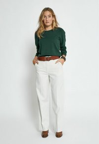 Pull vert à manches longues, pantalon blanc ample, ceinture marron avec boucle circulaire, bottines marron. Design simple, texture lisse.