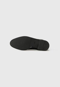 Semelle noire d'une chaussure avec une texture lisse, un bout légèrement arrondi et un motif de semelle minimal. Présente un logo de marque près de la zone du talon.
