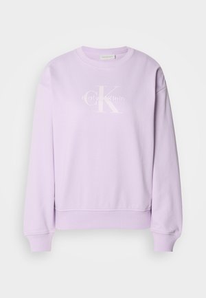 Fialová mikina vyrobená z mäkkého materiálu. Má okrúhly výstrih, dlhé rukávy, rebrované manžety a biele logo Calvin Klein na prednej strane.