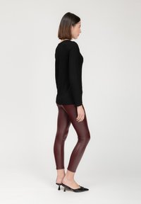 Schwarzes langärmliges Oberteil, figurbetonte bordeauxrote Leggings und schwarze Absatzmules. Glatter Stoff, schlanke Silhouette und minimalistisches Design.