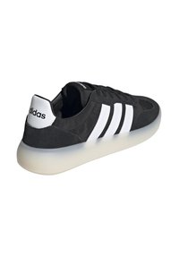 Sneaker nera con tre strisce bianche, materiale scamosciato, punta arrotondata, colletto imbottito e suola semitrasparente di colore chiaro.