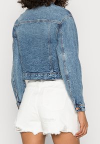 Back view of person wearing a cropped blue denim jacket and high-waisted white distressed shorts.