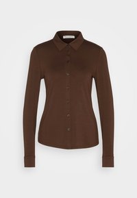 Chemise marron foncé à manches longues, boutonnée, avec col et taille ajustée, présentée sur un fond clair uni.