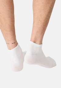 Witte enkelsokken, gebreide textuur, naadloos ontwerp, licht elastisch aan de boord, subtiel patroon aan de onderkant, gedragen op blote voeten met zichtbare beenharen.