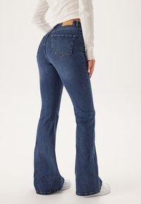 Uiteinde blauwe denim jeans met een medium taille, voorzien van twee achterzakken en een gestikte zoom. De stof heeft een zachte, duurzame textuur.