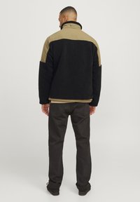 Giacca in pile nera con accenti khaki, colletto alto e vestibilità rilassata. Dettaglio notevole include R.D.D. ricamato sul retro.