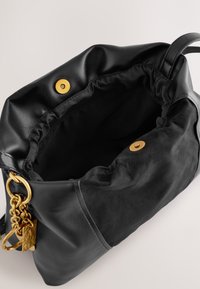 Mustast nahast käekott, millel on pehme ja lõdvestunud disain. Omab kuldset klõpskinnitust ning dekoratiivset kullast ketti, millel on tekstuurse detailiga ripats.