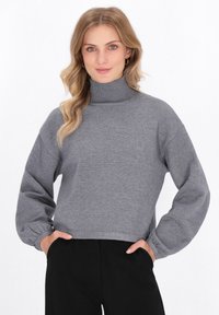 Grauer Rollkragenpullover mit einem cropped Design, Ballonärmel, gerippten Bündchen und einer glatten Textur, kombiniert mit schwarzen Hosen.