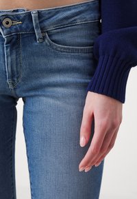 Tunna ljusblå denimjeans med en klassisk femfickedesign och subtila slitningar, i kombination med en ribbad marinblå tröja med ärm.