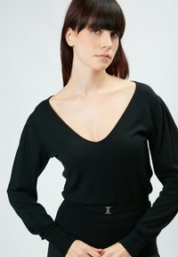 Maglione nero lavorato a maglia con scollatura a V profonda, maniche lunghe e polsini a coste. Presenta una vita aderente con dettagli in fibbia metallica.