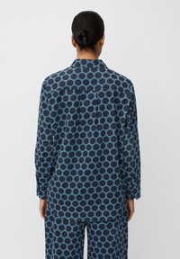 Camicia blu a pois con maniche lunghe, design con colletto e polsini a bottone. Realizzata in tessuto testurizzato con una vestibilità rilassata e dettaglio sul retro.