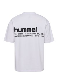Vit t-shirt med svart tryckt text på baksidan, inklusive varumärkesnamnet "hummel" och produktinformation. Korta ärmar, normal passform.