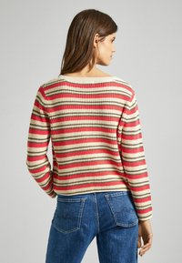 Maglione a righe in crema, rosso e grigio. Tessuto a maglia con scollatura ampia e maniche lunghe, abbinato a jeans in denim blu.