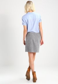 Chemise légère bleu clair à manches courtes associée à une jupe grise, mettant en valeur une texture lisse et un design ajusté. Des bottines brunes à la cheville complètent la tenue.