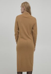 Rochie midi tricotată maro cu guler înalt, mâneci lungi și tiv cu nervuri. Textură moale și siluetă ajustată pentru un aspect elegant.