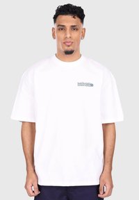 T-shirt en coton blanc à manches courtes, avec un petit imprimé graphique bleu sur la zone gauche de la poitrine. Coupe décontractée et design à col rond.