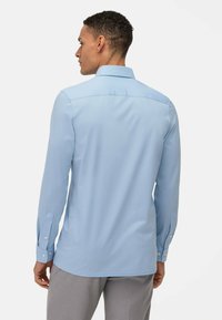 Lichtblauw langemouw shirt met een puntkraag, knoopmanchetten en een gladde textuur, weergegeven vanaf de achterkant.