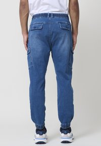 Denim hlače za prostočasne aktivnosti z elastičnim pasom, zoženimi manšetami, dvema stranskima žepoma in dvema zadnjima žepoma, v srednje modrem pranju z rahlo teksturo.
