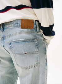Világoskék farmernadrág egy "TOMMY JEANS" felirattal ellátott bőrpanggal. Kis logó található a hátsó zsebben, és a textúrája fakult.