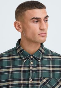 Grønternet flannel skjorte med knap-ned krave, som har sorte og beige striber, samt en brystlomme. Let vævet stof.