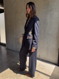 Jūrinio stiliaus smėlio dryžuotas kostiumas su pritaikytu švarku, kuriame ant kišenių išsiuvinėti akys ir saulė, derinamas su plačia kojų kelnėmis ir smėlio spalvos nertomis kulkšnimis.