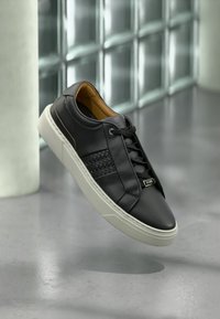 Scarpe da ginnastica nere in pelle con un dettaglio intrecciato testurizzato, suola piatta in gomma bianca, lacci neri e un piccolo logo argentato sul lato.