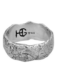 Anello in argento con una superficie textured e irregolare, caratterizzato da un bordo ondulato e timbrato con "925" che indica argento sterling e un logo.