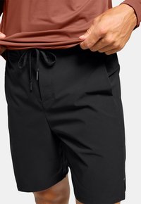 Shorts noirs en tissu léger, dotés d'une taille avec cordon de serrage, de poches latérales et d'une texture lisse.