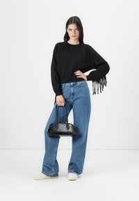 Felpa nera corta con dettagli di frange, abbinata a jeans a vita alta blue a gamba larga, mentre tiene una piccola borsa nera.