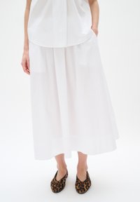 White, flowing, knee-length skirt with a smooth texture and wide silhouette. Worn with leopard-print flat shoes.