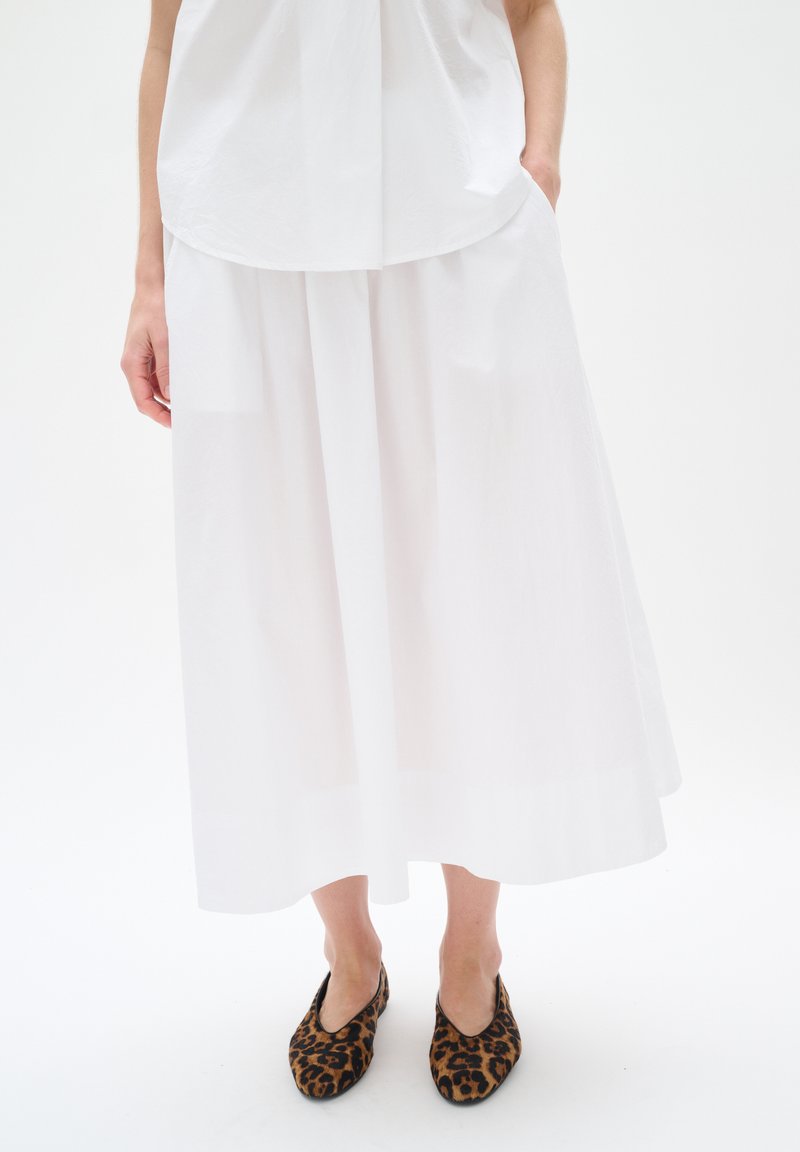 White, flowing, knee-length skirt with a smooth texture and wide silhouette. Worn with leopard-print flat shoes.
