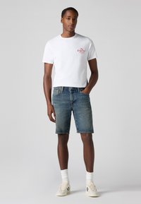 Șorturi scurte din denim de culoare albastră, cu o ușoară decolorare la coapse. Asortate cu un tricou alb cu text roșu. Adidași cu accente verzi.