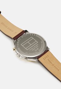 Orologio in acciaio inossidabile con quadrante argentato, cinturino in vera pelle marrone e dettagli incisi sul retro e sul cinturino. Impermeabile fino a 5 bar.