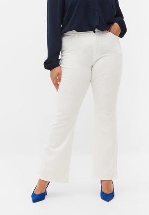 Pantalones acampanados blancos con una textura suave, combinados con una camisa de manga larga azul marino y tacones altos azules. El conjunto destaca por un look limpio y moderno.