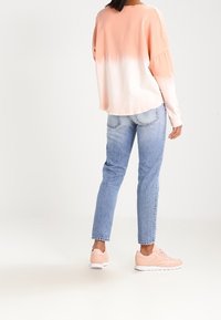 Lichtroze ombré sweater met een losse pasvorm, gecombineerd met blauwe jeans met rechte pijpen en lichtroze sneakers met witte zolen.