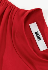 Rode stof met een gladde textuur en een geraffineerde halslijn. Het label toont de merknaam "BENU" in zwart op een witte achtergrond.