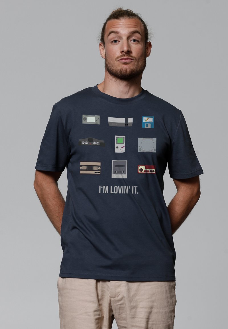 Navy t-shirt featuring pixel art of vintage gaming consoles, with the text "I'M LOVIN' IT." in white. Short sleeves, regular fit.