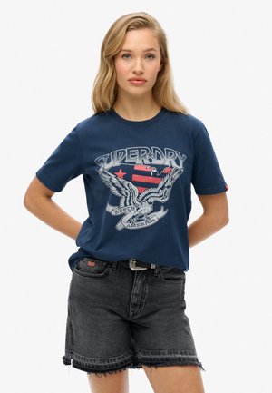 T-shirt en coton bleu marine avec un design d'aigle graphique, présentant le texte "SUPERDRY" et "NORTH AMERICA" en dessous. Col rond.